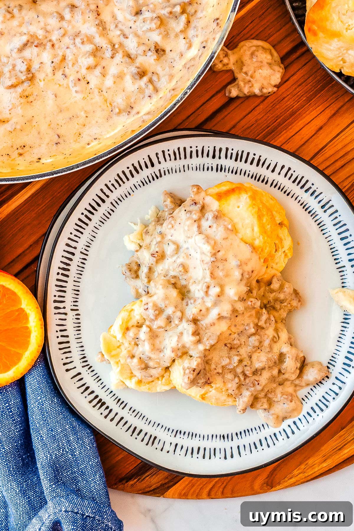 Biscuits and gravy on a plate with more gravy in a pan in the background.