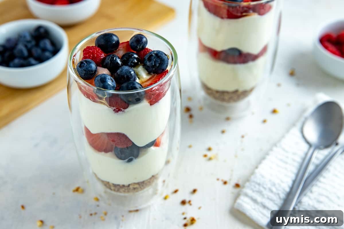 Layered Mixed Berry Parfaits with Greek Yogurt and Granola 6 Two tall clear glasses with a granola crust at the bottom, two layers of yogurt and two layers of strawberries and blueberries.