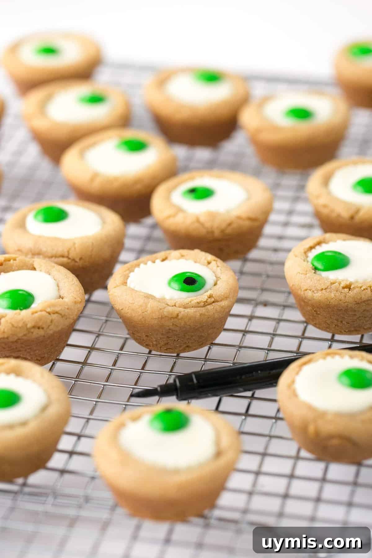 Halloween Eyeball Cookies with Peanut Butter Cups 11 Mini white peanut butter cup cookies on wire cooling rack with black food pen.