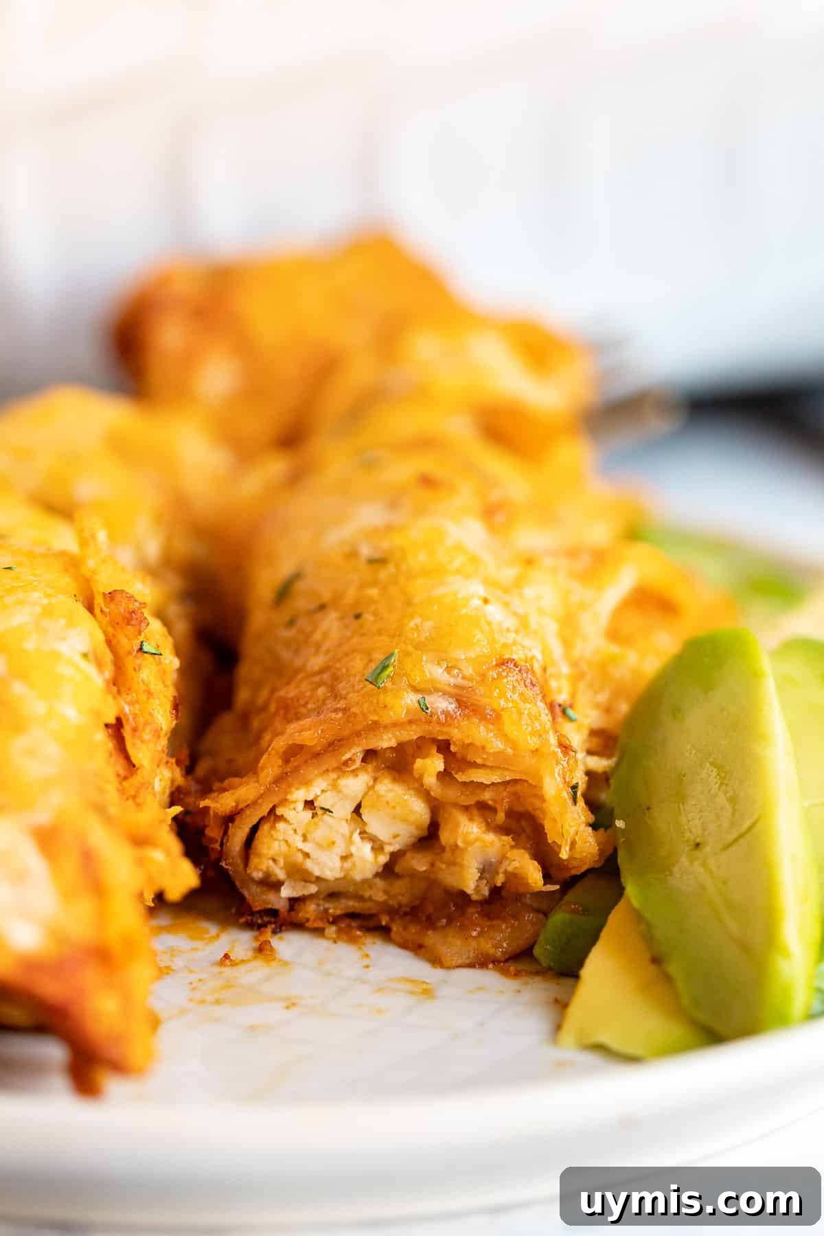 A close up image of an enchilada cut in half revealing the creamy chicken inside.