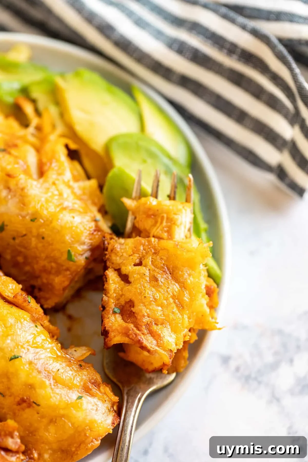A close up of a bite of enchiladas on the plate next to the rest of them.