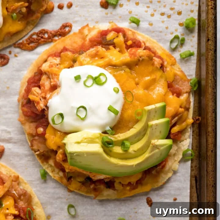 An overhead image of a chicken tostada on the pan with sour cream and avocado on top.