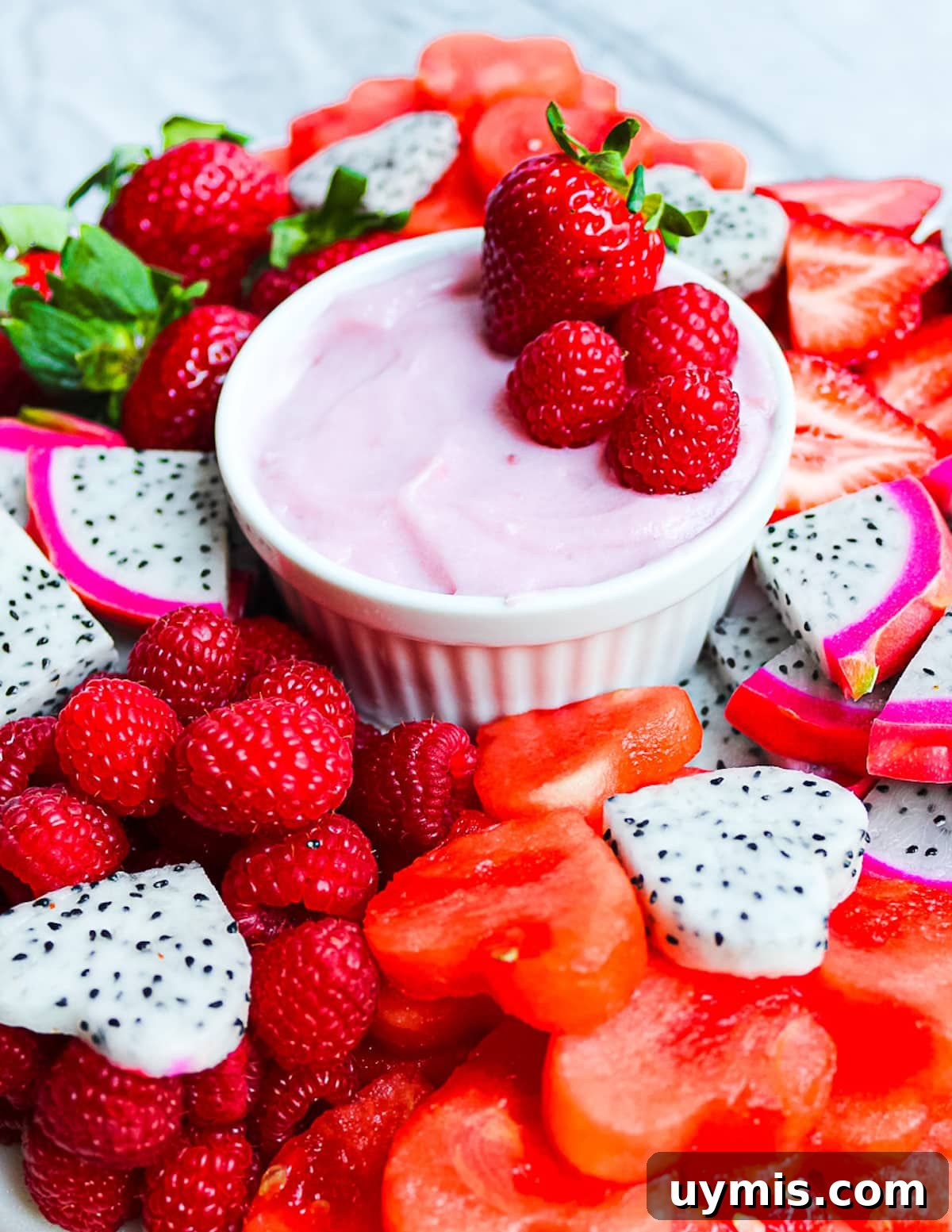 Creamy Vegan Fruit Dip Recipe for Fresh Fruit Platters 2 A platter of dragonfruit, strawberries, watermelon, and raspberries with a small white dish filled with a homemade strawberry fruit dip.