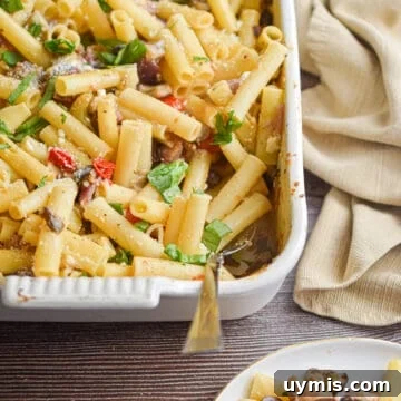 A napkin is behind the baking dish with the Greek Pasta Bake in it and a portion is on a plate in front of the baking dish.