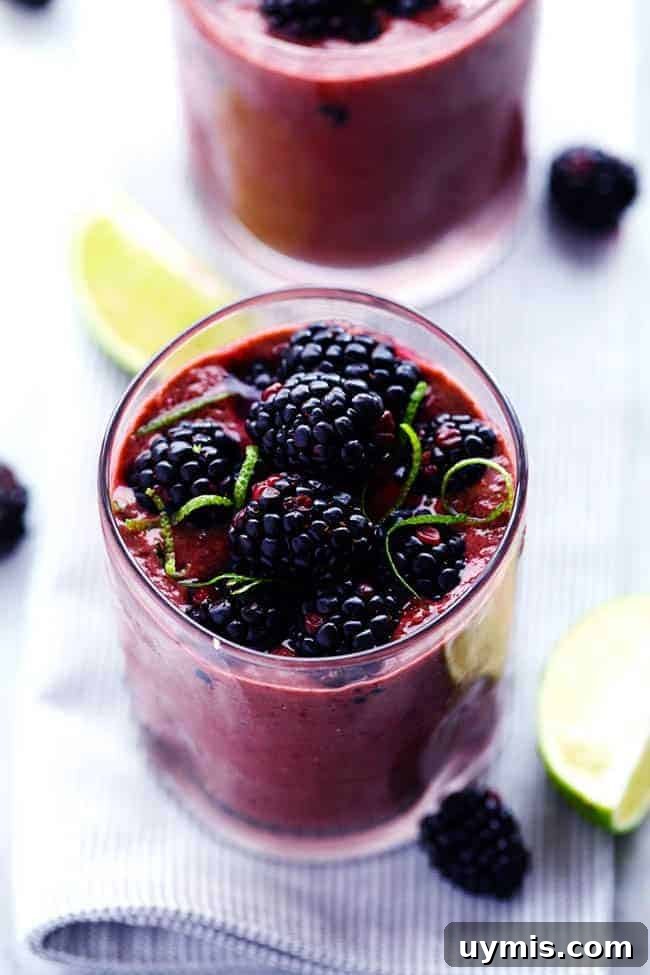 Creamy blackberry lime green smoothie served with fresh lime and blackberries. Close-up photo of blackberry lime smoothie in a clear glass with fresh limes and blackberries on the side.