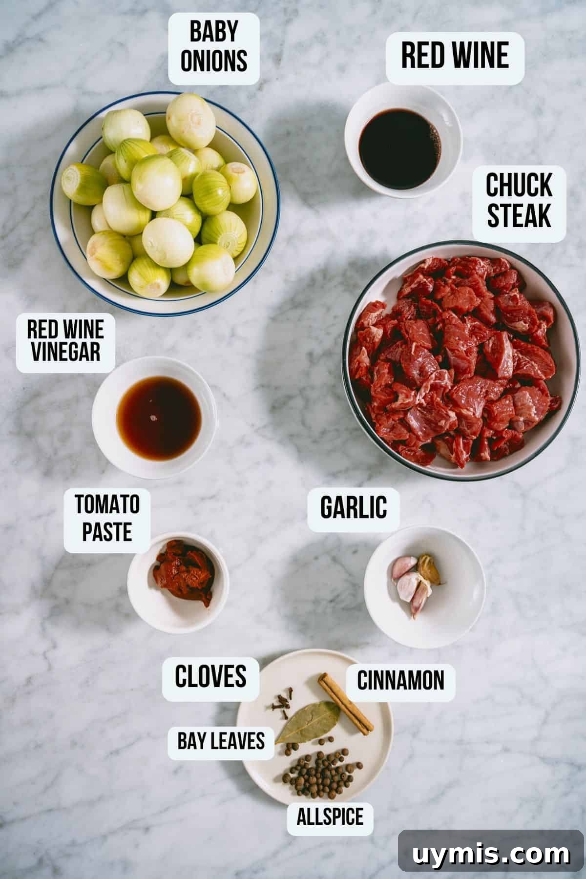 Greek Beef Stifado Recipe: Classic Slow-Braised Stew 4 The ingredients to make beef stifado on a white marble table.