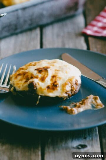 Ground beef stuffed portobello mushroom topped with melted cheese served on a blue plate.