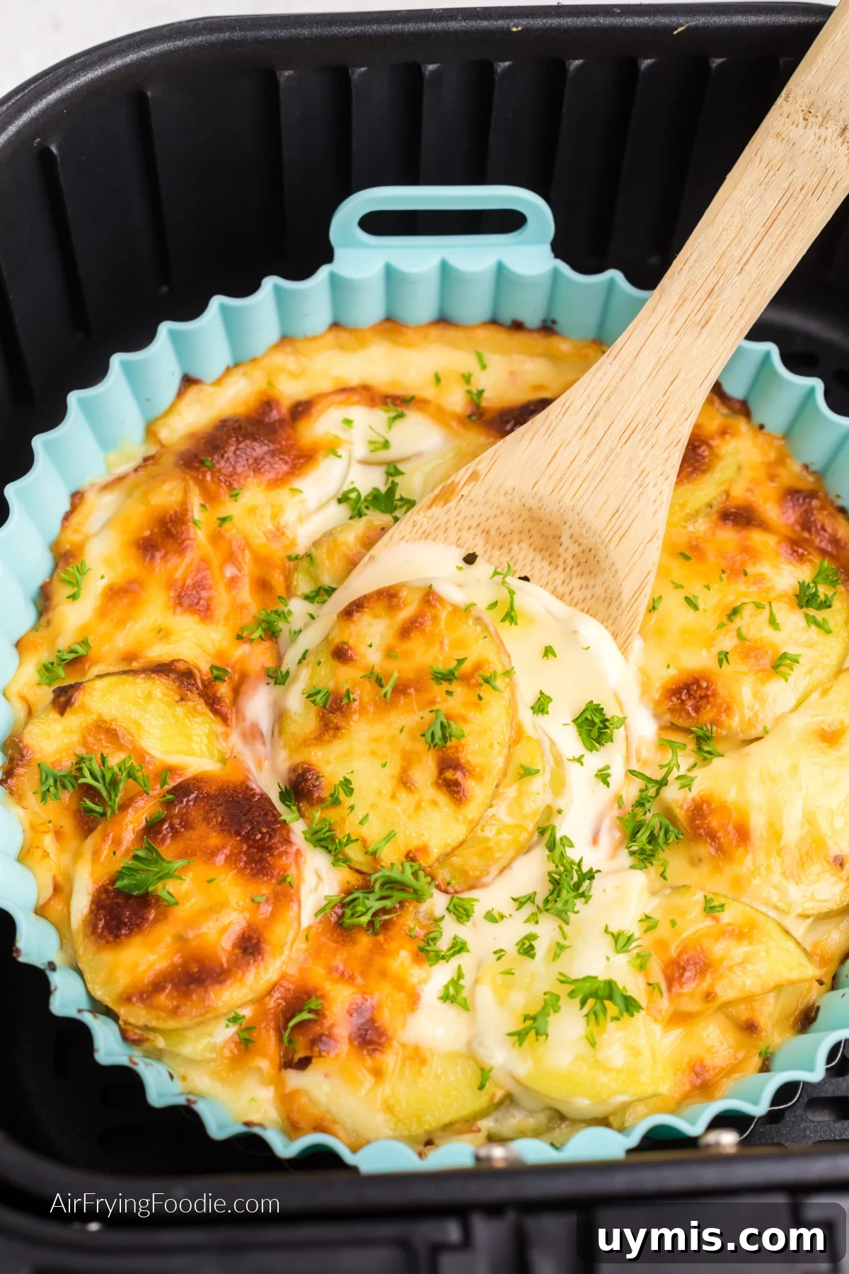 Air Fryer Scalloped Potatoes with Melted Cheese 11 Air fryer scalloped potatoes topped with fresh parsley and a wooden spoon scooping out a serving.
