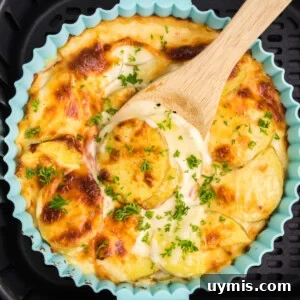 Air Fryer Scalloped Potatoes with Melted Cheese 14 Cheesy scalloped potatoes being scooped from the dish in the basket of the air fryer.