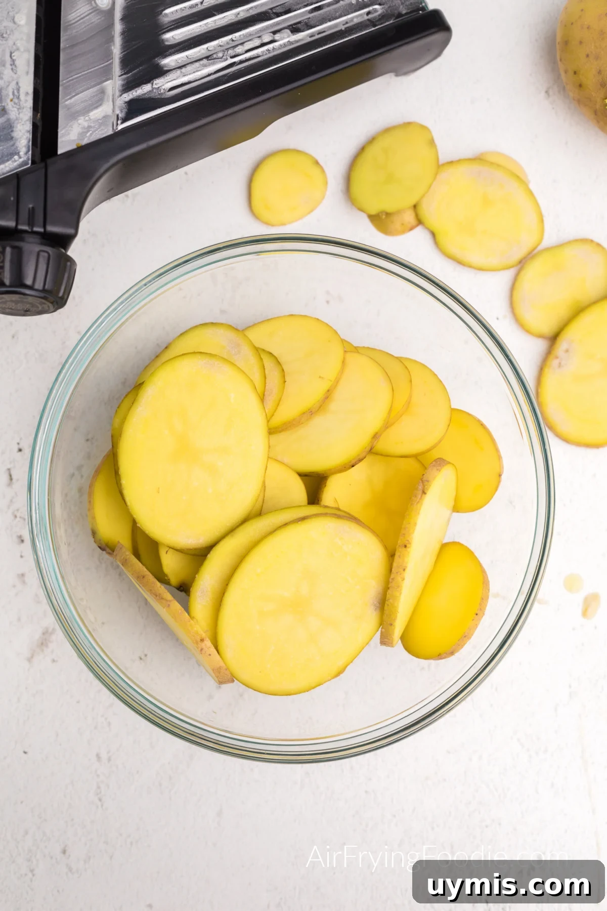 Air Fryer Scalloped Potatoes with Melted Cheese 4 Potatoes in a bowl that have been sliced with a mandolin.