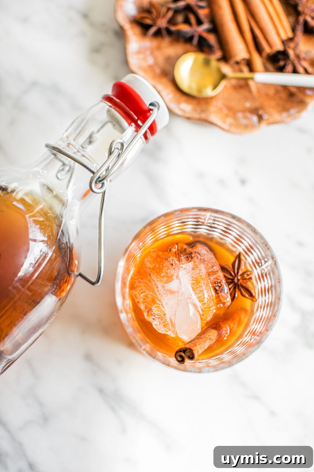 an overhead photo of an old fashioned in a lowball glass with star anise and a cinnamon stick as garnish, and a swing top bottle over it