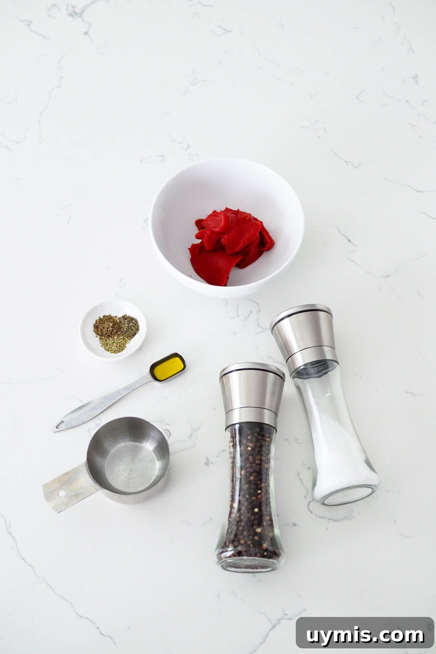 How to Make Pizza Sauce from Tomato Paste 3 Tomato paste, salt and pepper, water, olive oil, and spices on a white counter.