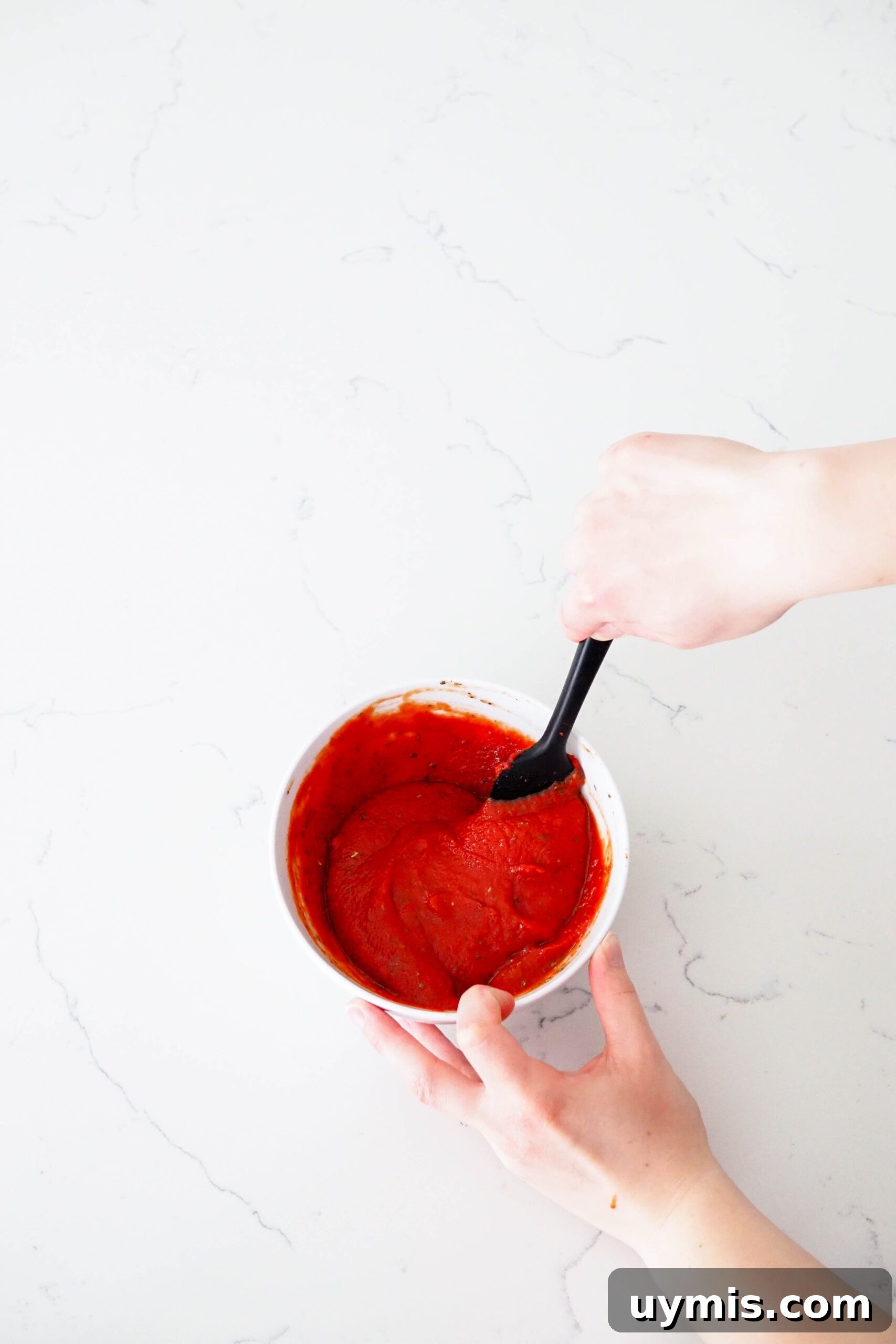 How to Make Pizza Sauce from Tomato Paste 5 A hand stirs together pizza sauce with a spatula.