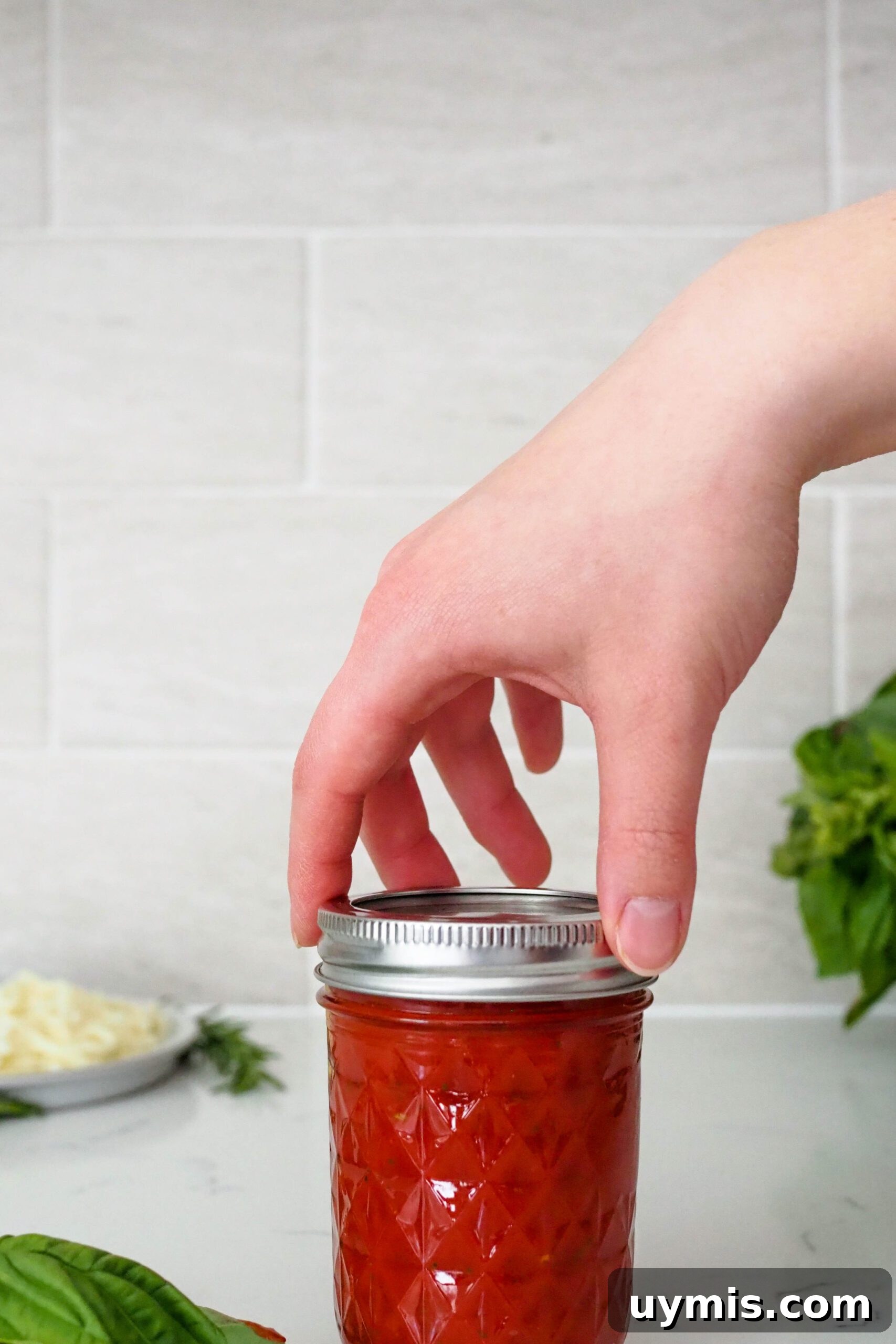 How to Make Pizza Sauce from Tomato Paste 6 A hand screws on the lid of a jar containing pizza sauce made from tomato paste.
