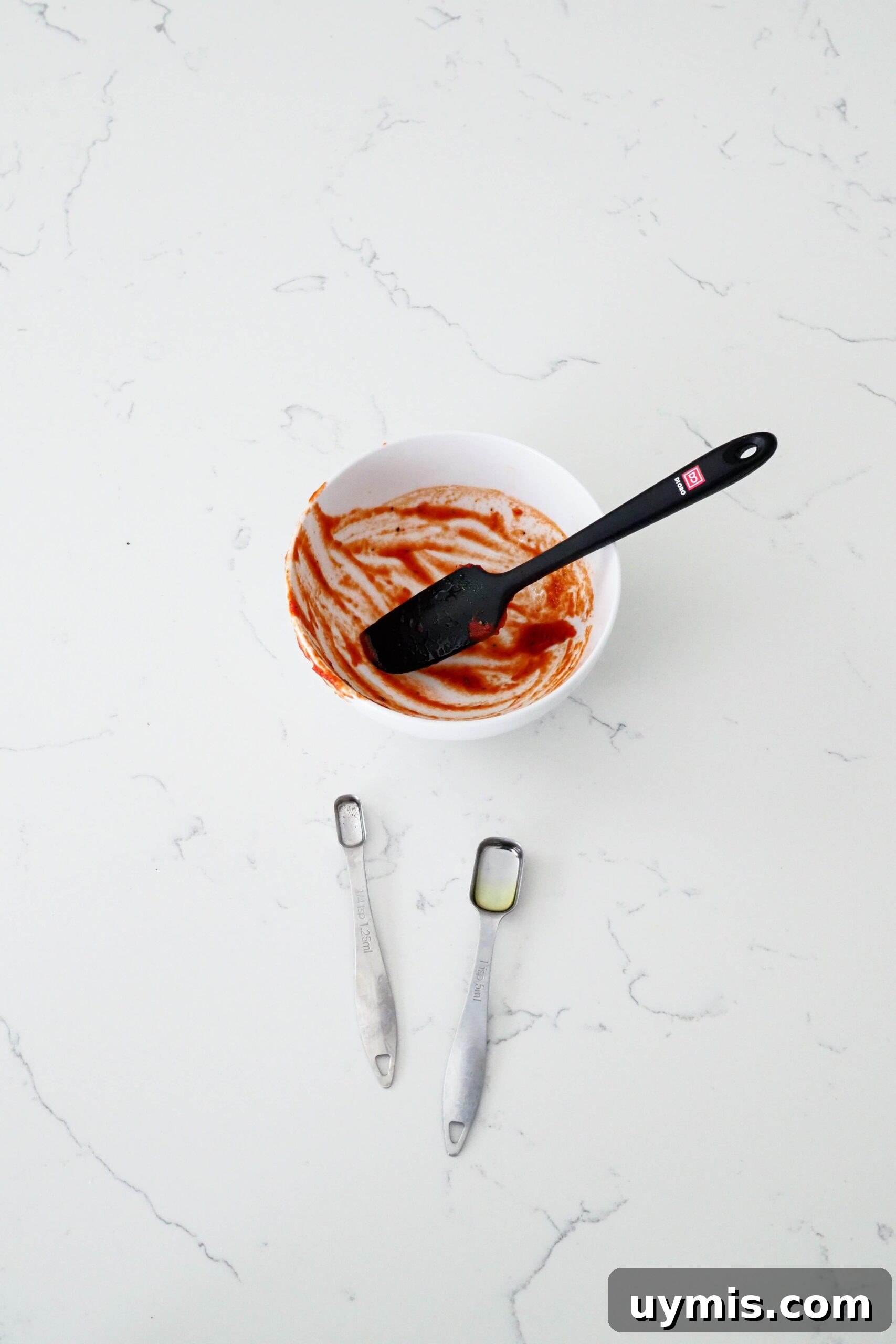 How to Make Pizza Sauce from Tomato Paste 7 A single bowl, spatula, and two measuring spoons on a quartz counter.
