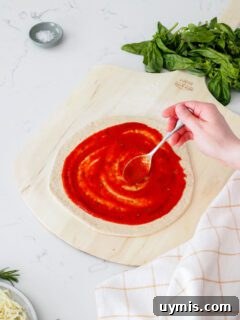How to Make Pizza Sauce from Tomato Paste 8 A hand spreads pizza sauce onto a round of pizza dough.