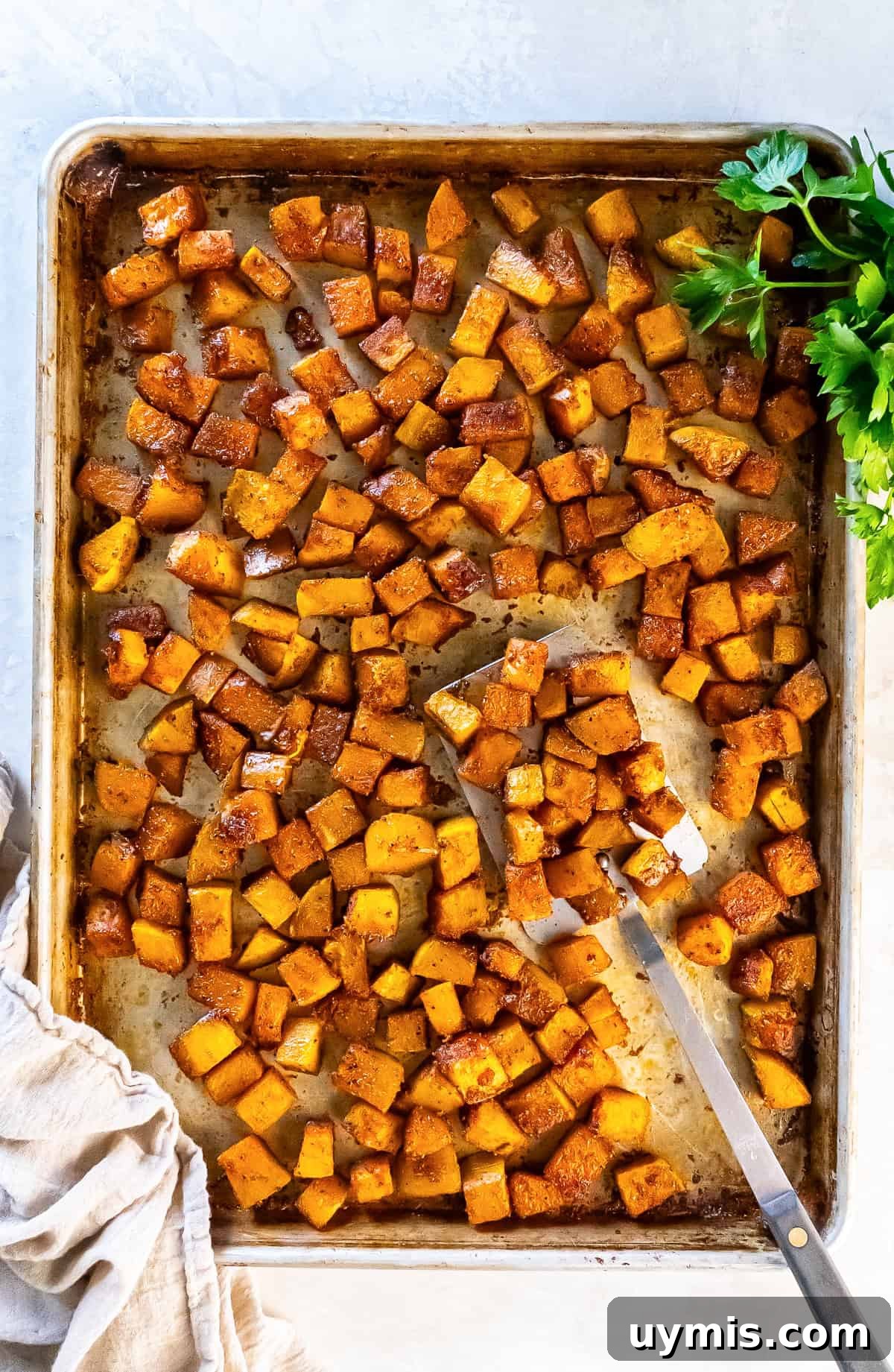 Spiced Roasted Butternut Squash Recipe 8 Roasted butternut squash cubes on a sheet pan with a spatula and parsley.