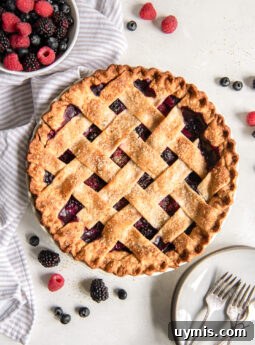 triple berry pie on tabletop with a bowl of fresh berries.