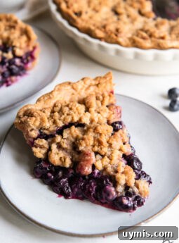 slice of blueberry crumble pie with juicy filling on round grey plate