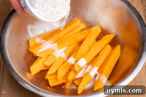 Crispy Air Fryer Sweet Potato Fries 9 Pouring cornflour slurry over par boiled sweet potato fries in a large silver bowl
