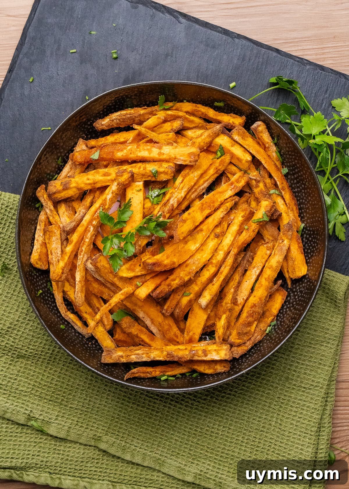 Crispy Air Fryer Sweet Potato Fries 19 Air fryer sweet potato fries in a large black bowl. with parsley sprinkled on top.