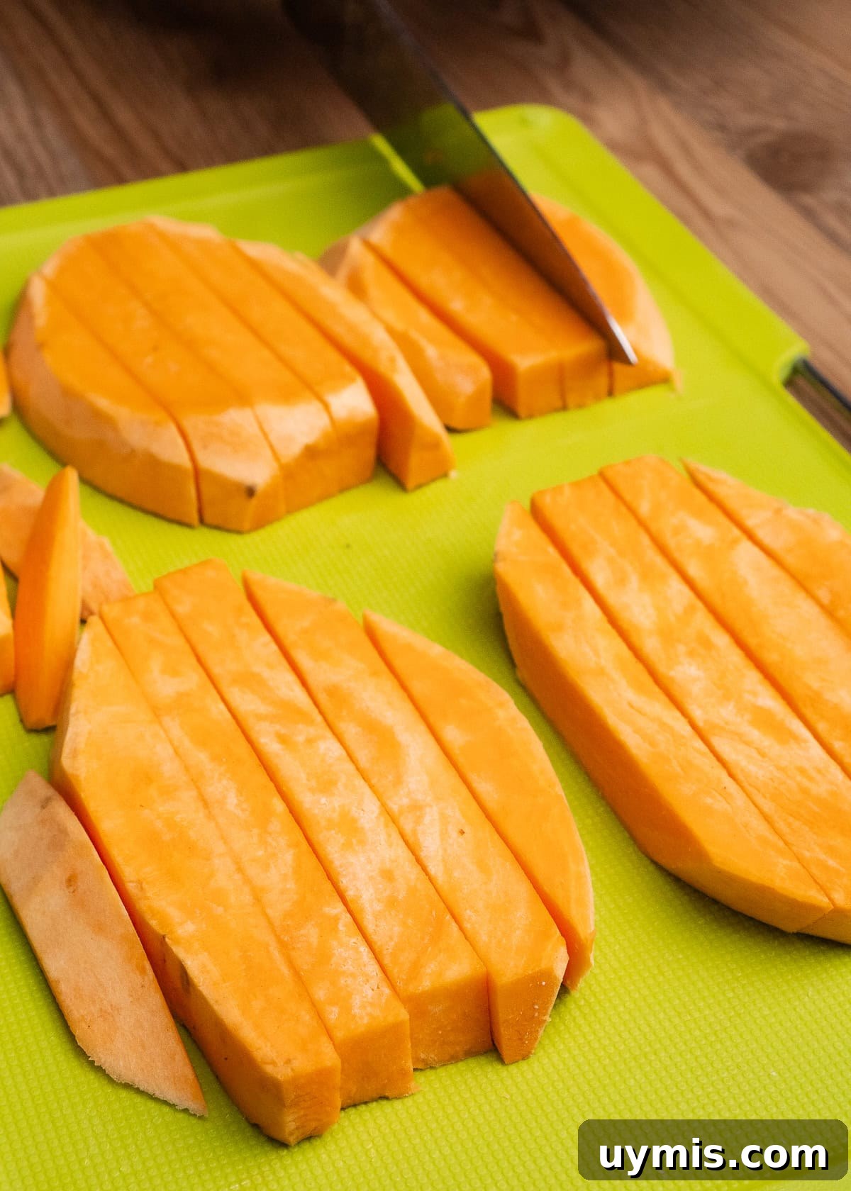 Crispy Air Fryer Sweet Potato Fries 22 Slicing sweet potato with a knife into strips on a green chopping board