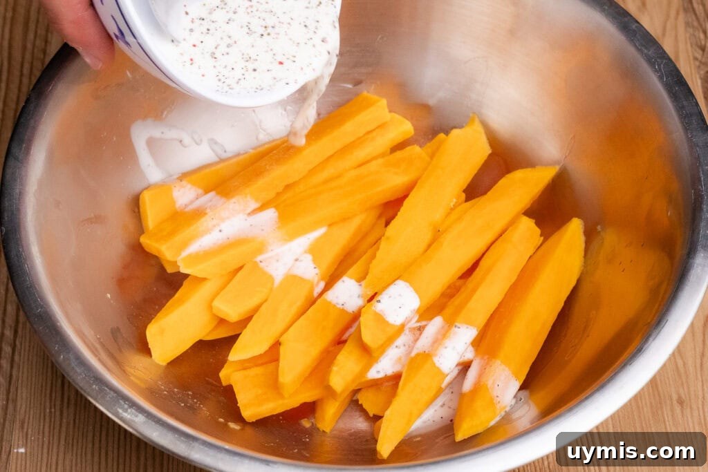 Crispy Air Fryer Sweet Potato Fries 26 Pouring cornflour slurry over par boiled sweet potato fries in a large silver bowl