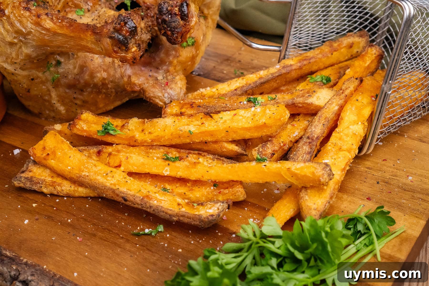 Crispy Air Fryer Sweet Potato Fries 31 Air Fryer Sweet Potato chips coming out of a silver basket with a whole cooked chicken served on the side on a wooden chopping board