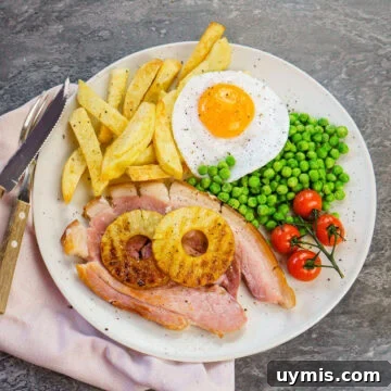 Gammon egg and homemade chips served with vined cherry tomatoes,peas and two pineapple rings on a white plate