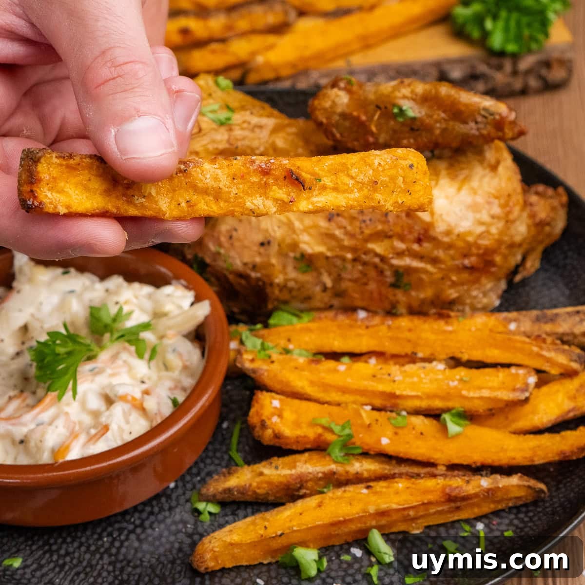 Crispy Air Fryer Sweet Potato Fries 38 Holding a sweet potato fries over a plate of chicken, coleslaw and air fryer sweet potato fries on a black plate
