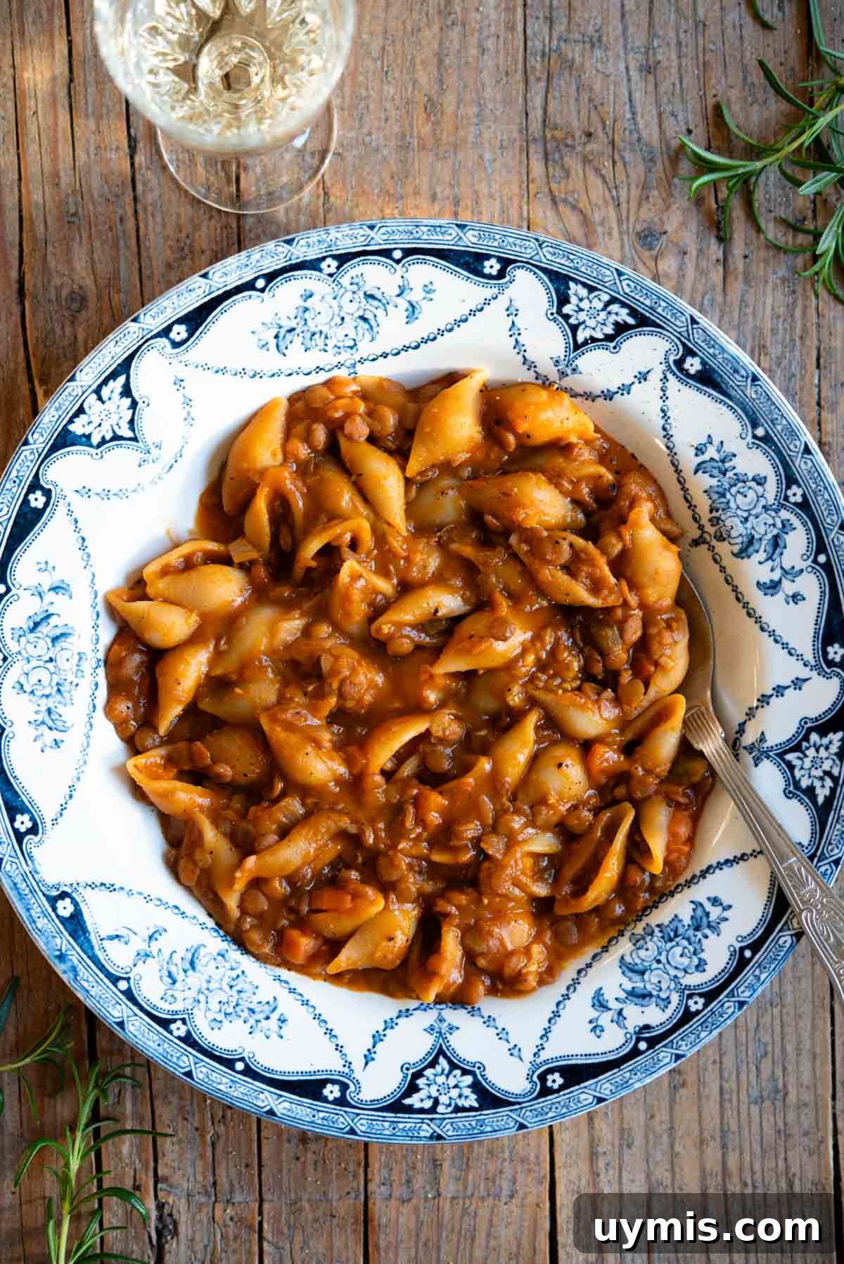 Pasta e Lenticchie Italian Pasta and Lentils Recipe 2 An overhead shot of pasta and lentils in a blue vintage style bowl on a rustic background with a glass of white wine at the side.