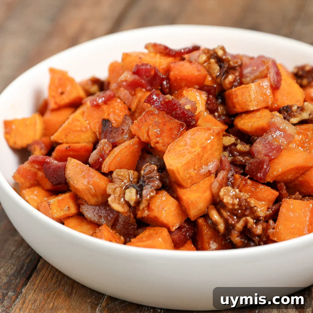 Maple Roasted Sweet Potatoes with Bacon and Walnuts 2 A white bowl filled with Maple Roasted Sweet Potato with Bacon & Walnuts sits on a wooden surface, featuring crispy bacon pieces and glazed walnuts.