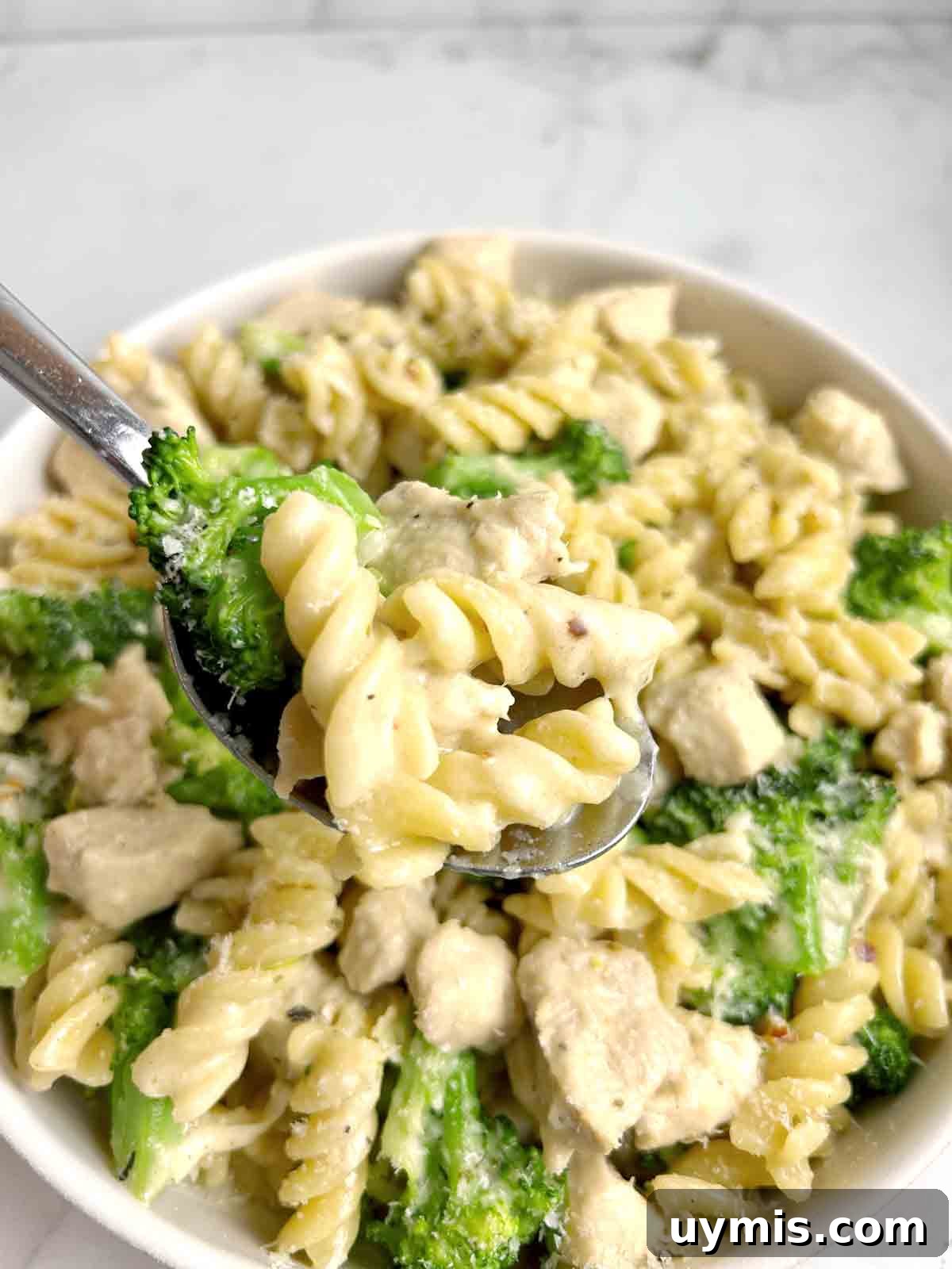 Creamy One Pot Chicken and Broccoli Pasta 8 spoon lifting chicken and broccoli pasta from plate.