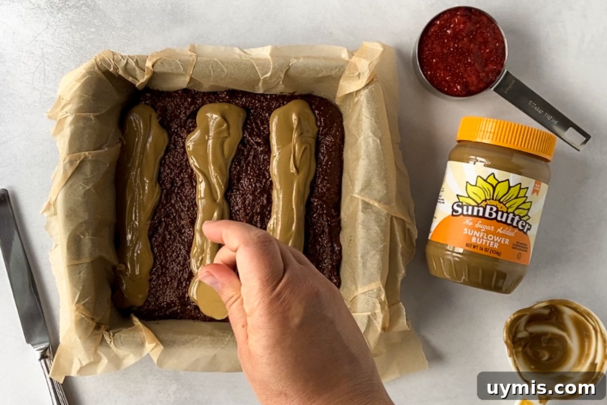 SunButter and Jelly Brownies 3 hand drizzling lines of SunButter on brownies in parchment lined pan