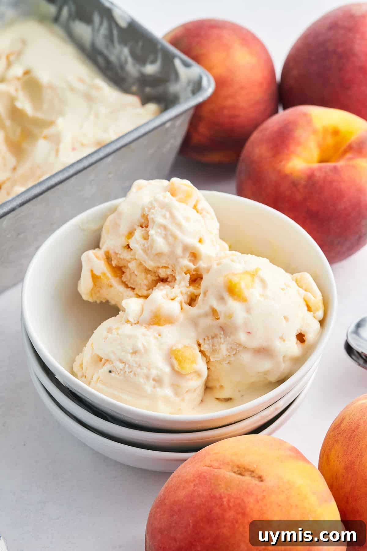 Homemade Peach Frozen Yogurt Recipe 3 Three scoops of peach frozen yogurt in a small white bowl surrounded by fresh peaches.