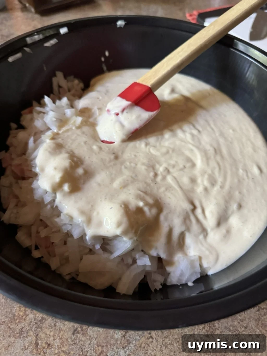 Baked Eggs Benedict Hash Brown Casserole 4 A pan of white sauce with chopped onions and a red spatula.