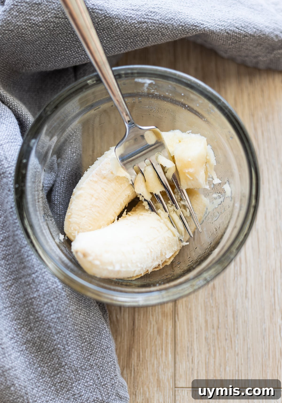 Fork smashing a banana in a bowl.