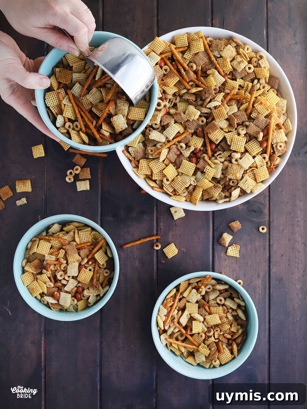 Crispy Oven Baked Chex Mix with Bacon Drippings 2 Hand using a metal measuring cup to measure out homemade chex mix into blue serving bowls.