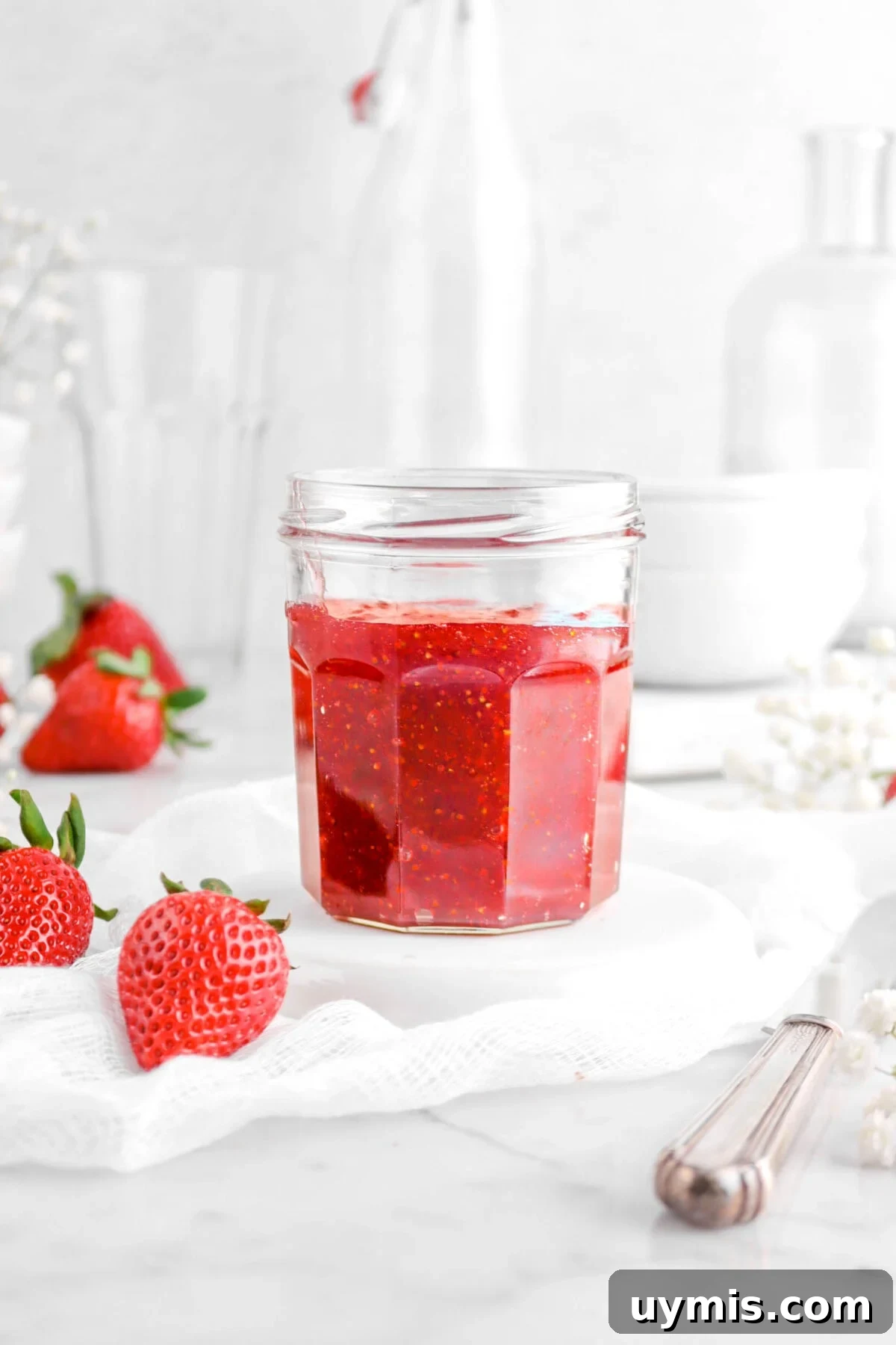 close up of jar of jam on upside down white plate with fresh strawberries beside