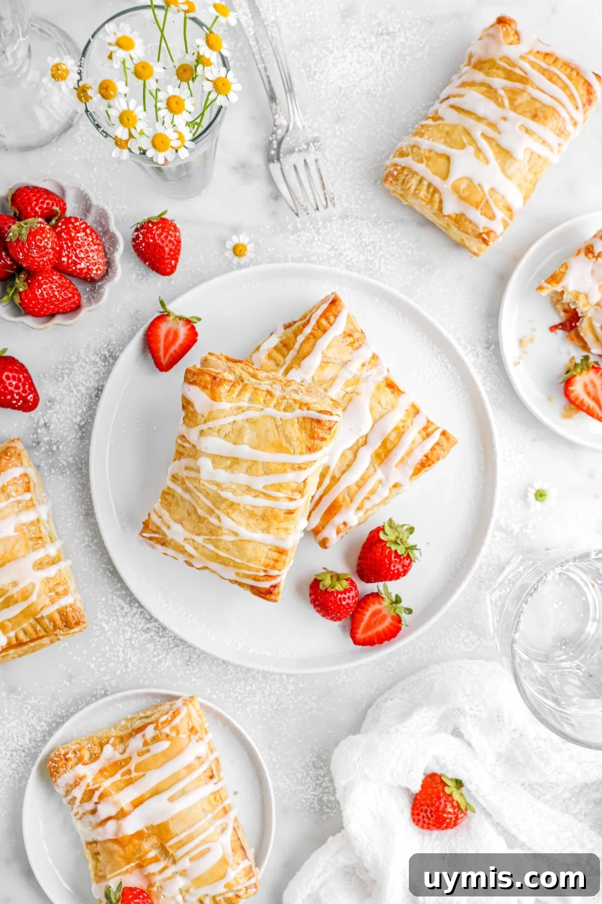 overhead image of toaster strudels on white plates and marble surface with flowers and strawberries around.