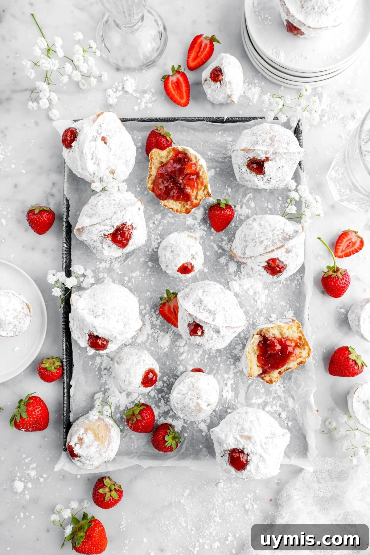 jelly filled muffins on parchment lined pan with strawberries and flowers around.
