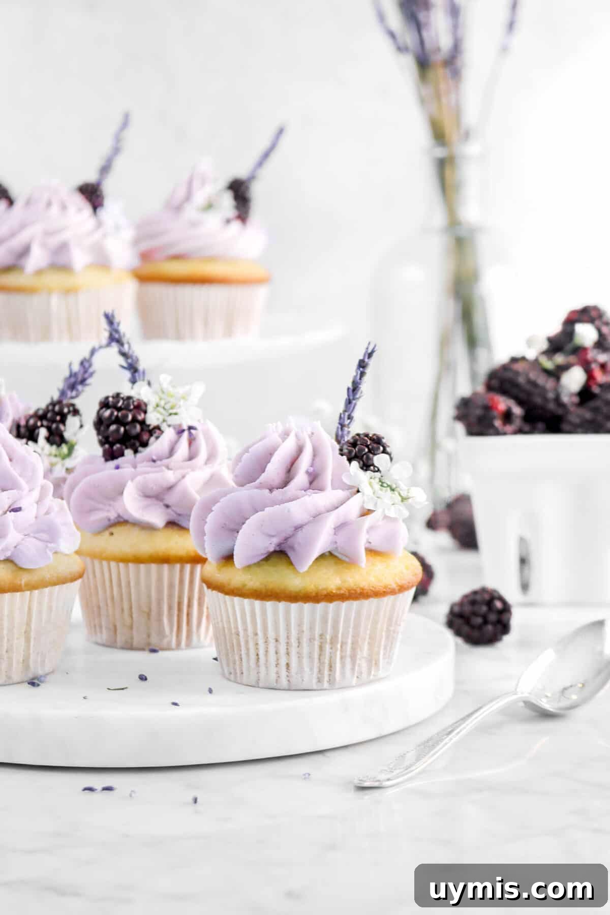 cupcakes on marble serving board with blackberries, lavender, white flowers, and a spoon