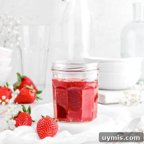 strawberry jam in glass jar on upside down white plate with white cheese cloth, silver knife, fresh strawberries, flowers, and empty glasses behind