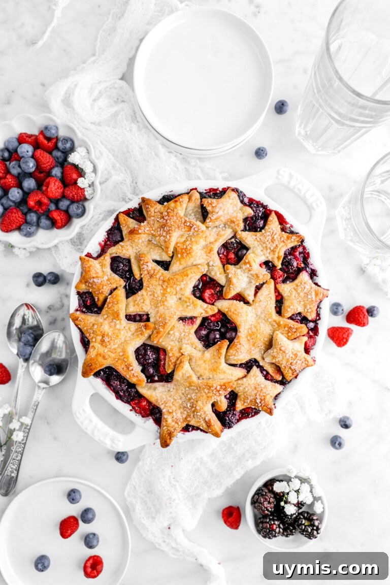 berry pandowdy on marble surface with berries, white flowers, and white plates around.