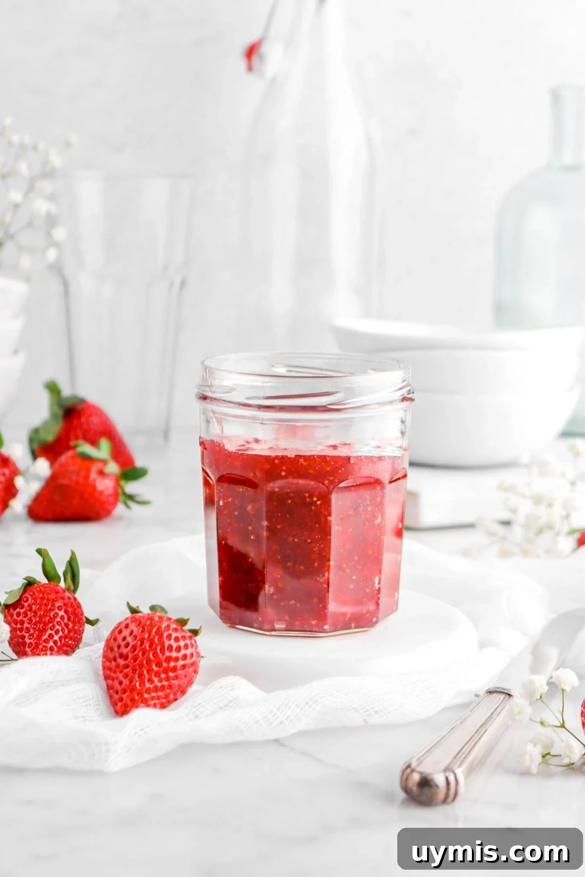 strawberry jam in glass jar on white plate with fresh strawberries around