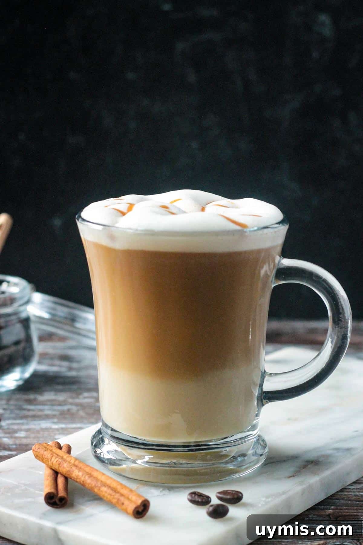 Apple crisp oatmilk macchiato in a glass topped with frothed milk and caramel drizzle.