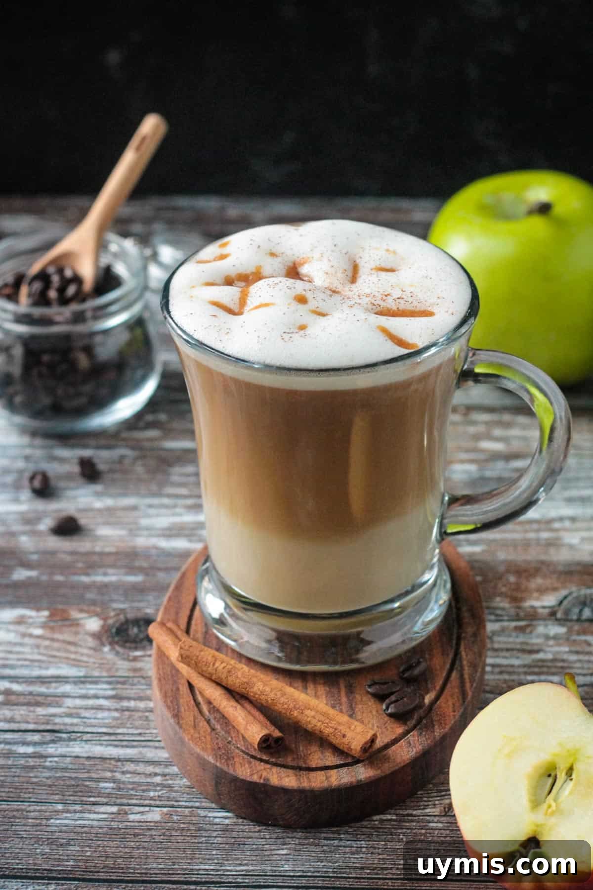 Apple coffee drink in a glass with two cinnamon sticks in front.