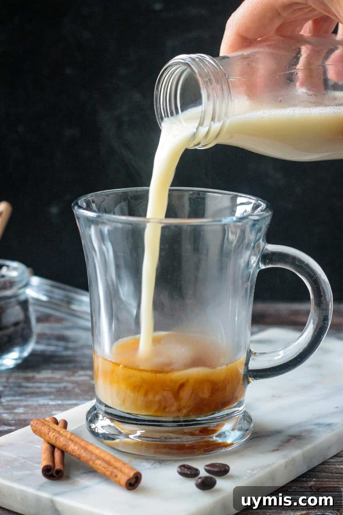 Pouring steamed milk over apple brown sugar syrup in a glass.