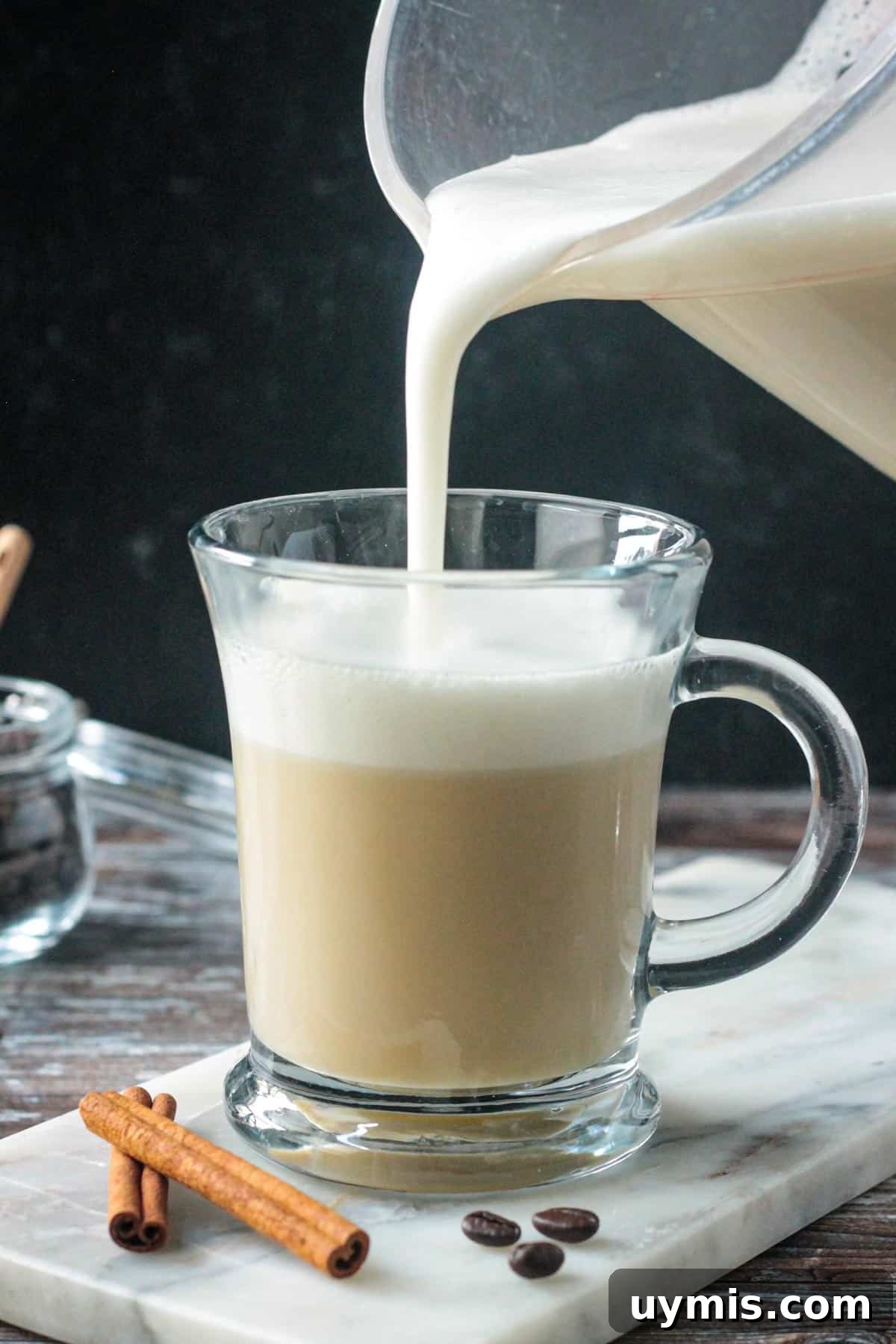 Pouring frothed milk on top of steamed milk and apple cider syrup in a glass.