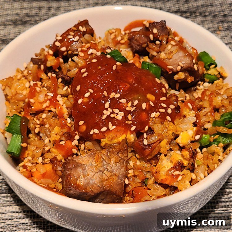 Teriyaki Steak Fried Rice served in a bowl with chili paste, siracha sauce, and sesame seeds